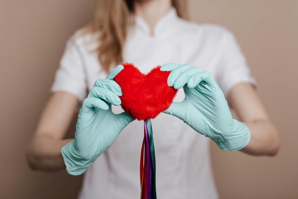 Close-up of a woman holding a red heart symbol with blue gloves and ribbons.